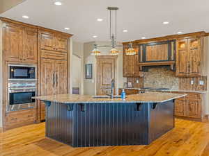 Kitchen featuring a kitchen bar, a sink, backsplash, light wood-style floors, and built in appliances