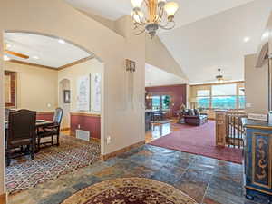 Dining space featuring visible vents, baseboards, stone tile floors, ceiling fan with notable chandelier, and high vaulted ceiling