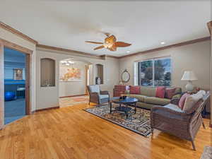 Living area featuring baseboards, ornamental molding, light wood-style floors, arched walkways, and a ceiling fan