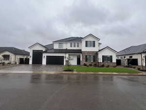 Modern farmhouse with brick siding, board and batten siding, a front lawn, decorative driveway, and a garage