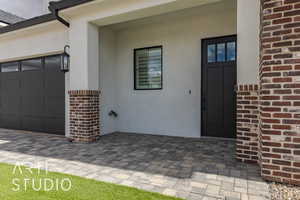 Doorway to property featuring brick siding, a garage, and stucco siding