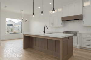 Kitchen with wall chimney range hood, a center island with sink, light wood-type flooring, white cabinets, and a sink