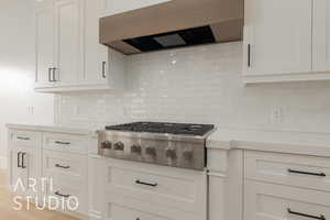 Kitchen featuring decorative backsplash, white cabinets, custom range hood, and stainless steel gas stovetop