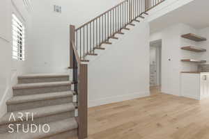 Stairway featuring a high ceiling, wood finished floors, visible vents, and baseboards
