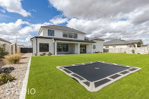 Back of property with stucco siding, a lawn, a trampoline, a fenced backyard, and a patio area