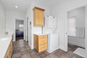 Ensuite bathroom with stone finish flooring, ensuite bath, stacked washer / dryer, baseboards, and vanity