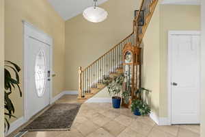 Tiled foyer entrance with stairway, baseboards, and a towering ceiling