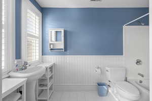 Full bath with tile patterned floors, a wainscoted wall, a wealth of natural light, and shower / bath combination