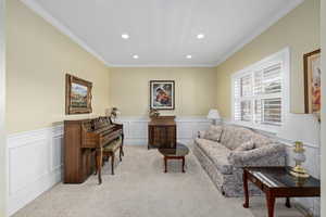 Living room with recessed lighting, light colored carpet, crown molding, and a wainscoted wall