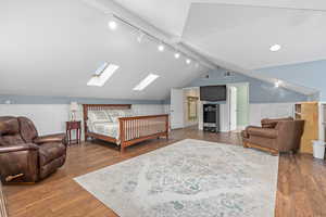 Bedroom with lofted ceiling with skylight, wood finished floors, visible vents, and track lighting