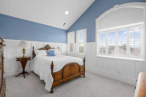 Carpeted bedroom featuring visible vents, lofted ceiling, wainscoting, and a decorative wall