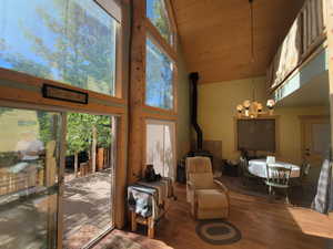 Living room with high vaulted ceiling, a notable chandelier, wood finished floors, wooden ceiling, and a wood stove
