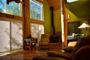 Living room featuring a wood stove, wood finished floors, and high vaulted ceiling