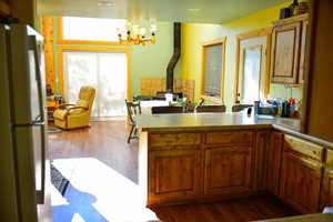 Kitchen featuring a notable chandelier, dark wood finished floors, freestanding refrigerator, a peninsula, and a wood stove