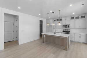 Kitchen featuring a center island with sink, a sink, stainless steel appliances, light countertops, and light wood-style floors