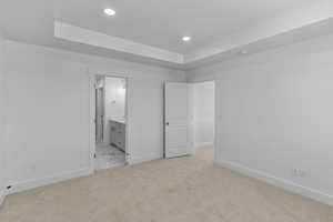 Unfurnished bedroom featuring light carpet, a tray ceiling, ensuite bath, recessed lighting, and baseboards