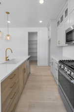 Kitchen featuring light wood-type flooring, a sink, decorative light fixtures, appliances with stainless steel finishes, and glass insert cabinets