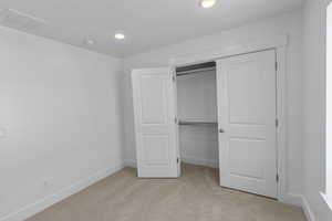 Unfurnished bedroom with visible vents, light carpet, baseboards, and a closet