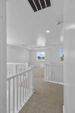 Hallway featuring an upstairs landing, visible vents, carpet flooring, and a textured ceiling