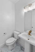 Half bathroom featuring baseboards, toilet, and marble finish floor