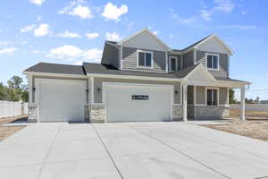 View of front of home featuring stone siding, board and batten siding, concrete driveway, and fence