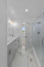 Bathroom featuring double vanity, a stall shower, a sink, a textured ceiling, and marble finish floor