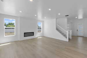 Unfurnished living room with light wood-style flooring, visible vents, a healthy amount of sunlight, and stairs