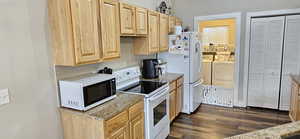 Kitchen with washing machine and clothes dryer, tasteful backsplash, light brown cabinets, dark wood-type flooring, and white appliances