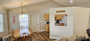 Dining area with dark wood-style floors, baseboards, and vaulted ceiling