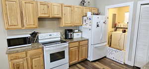 Kitchen with white appliances, dark wood-style floors, light brown cabinetry, decorative backsplash, and washer and dryer