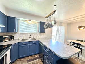 Kitchen with a peninsula, blue cabinets, dark wood-style flooring, a sink, and appliances with stainless steel finishes