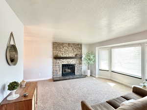 Carpeted living area with a textured ceiling, a fireplace, and baseboards
