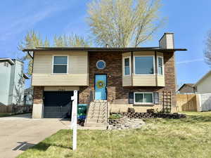 Bi-level home with a garage, a chimney, fence, concrete driveway, and a front lawn