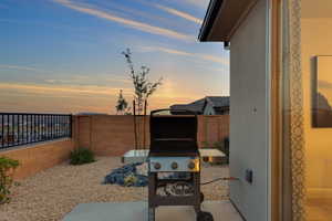 Patio terrace at dusk featuring fence and a grill