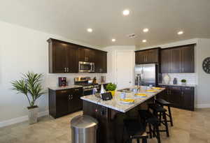 Kitchen featuring visible vents, a sink, stainless steel appliances, a breakfast bar area, and dark brown cabinets