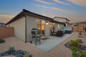 Back of property at dusk featuring stucco siding, a patio, a fenced backyard, and a hot tub