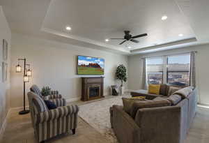 Living room with baseboards, ceiling fan, recessed lighting, a fireplace, and a raised ceiling