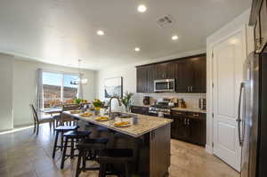 Kitchen featuring visible vents, a sink, light stone counters, appliances with stainless steel finishes, and decorative backsplash