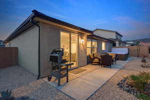 Back of property at dusk featuring stucco siding, a patio area, a fenced backyard, and a hot tub