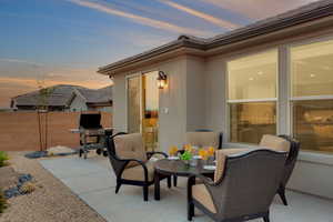 Patio terrace at dusk featuring outdoor dining area, fence, and a grill