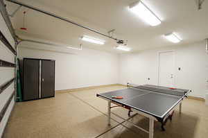 Game room with a garage, light speckled floor, and baseboards