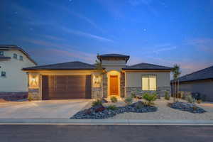 Prairie-style house with stucco siding, stone siding, an attached garage, and driveway