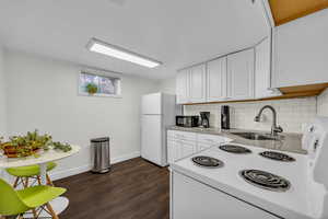 Kitchen featuring dark wood finished floors, white appliances, white cabinetry, and a sink