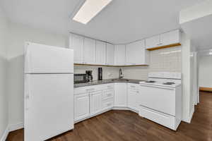 Kitchen featuring dark wood-style floors, white cabinets, white appliances, and a sink