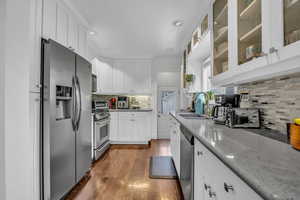 Kitchen with light stone countertops, dark wood finished floors, stainless steel appliances, white cabinetry, and a sink