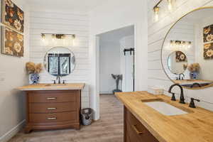 Full bathroom with a sink, two vanities, wood finished floors, and wood walls