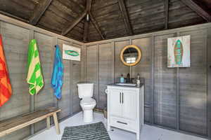 Bathroom with toilet, wooden ceiling, wood walls, vanity, and vaulted ceiling