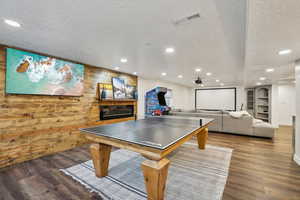 Game room featuring visible vents, wood finished floors, a glass covered fireplace, and wood walls