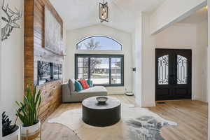 Entrance foyer featuring vaulted ceiling, french doors, light wood-style floors, and a textured ceiling