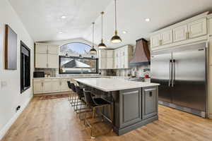 Kitchen featuring stainless steel built in refrigerator, light countertops, custom range hood, vaulted ceiling, and light wood-style floors